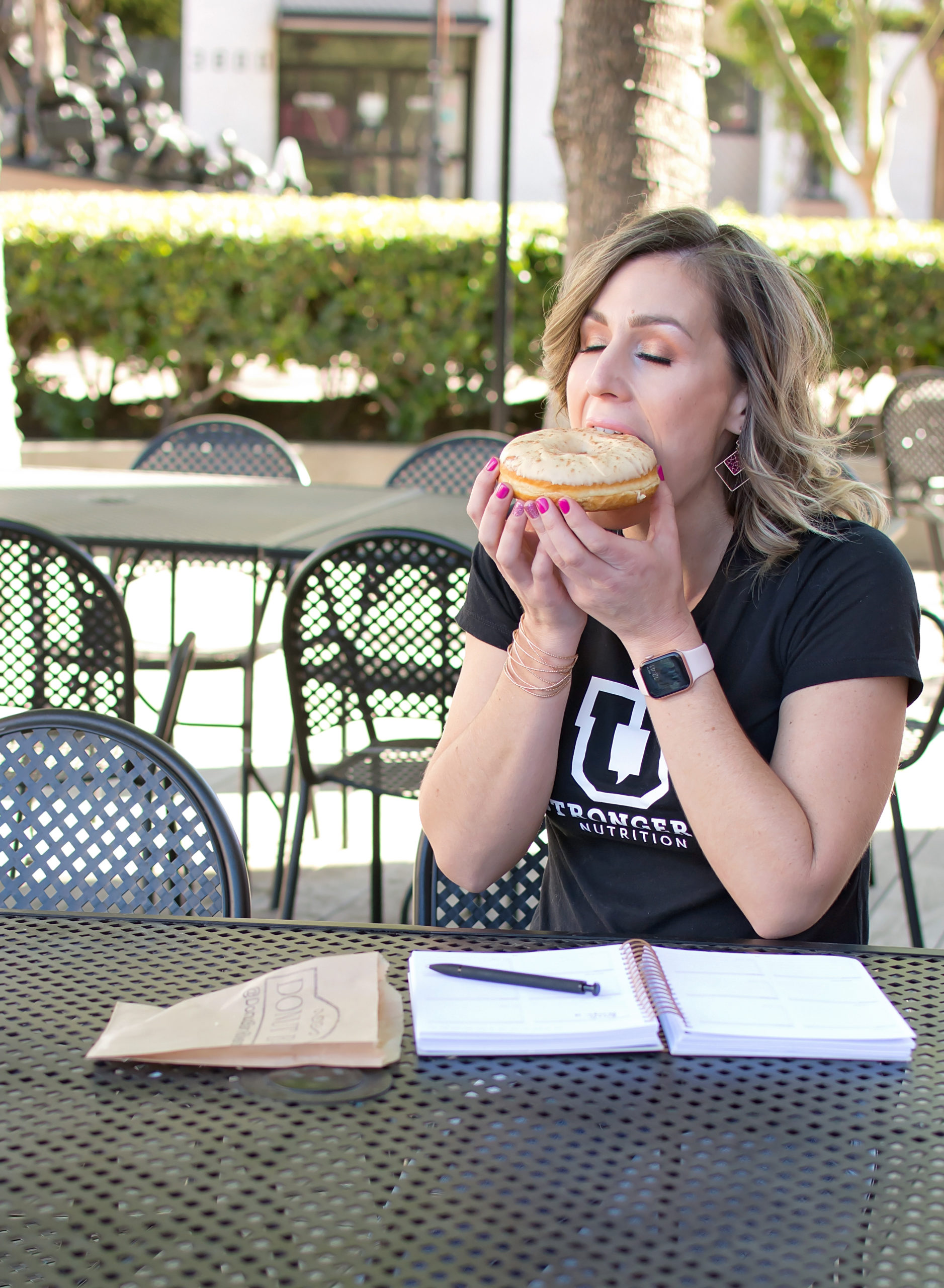 Fitness and Nutrition Coach eating a donut in downtown in a black shirt with a planner