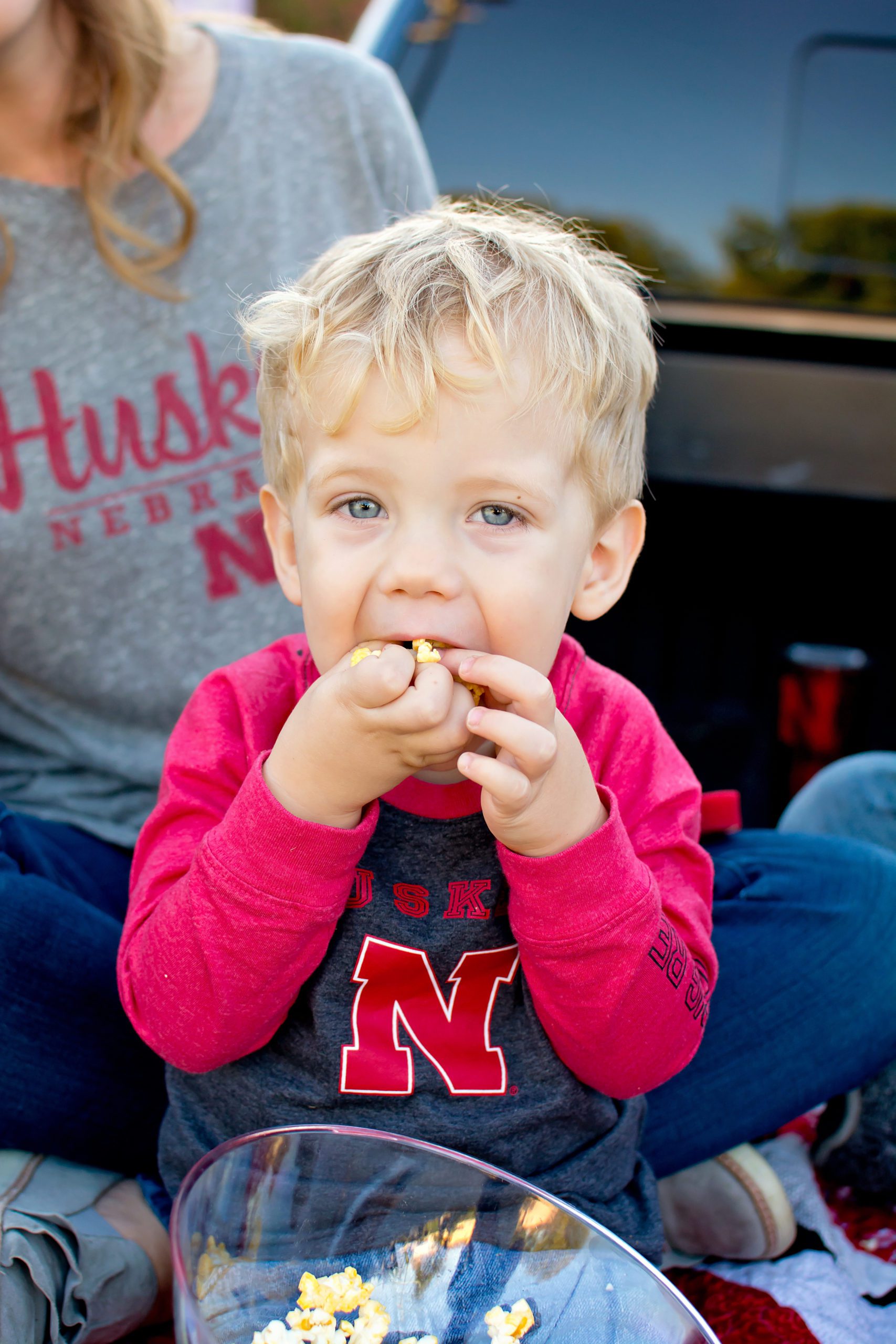 Riverside Family Photographer. Little boy in a Nebraska shirt stuffing his face with popcorn